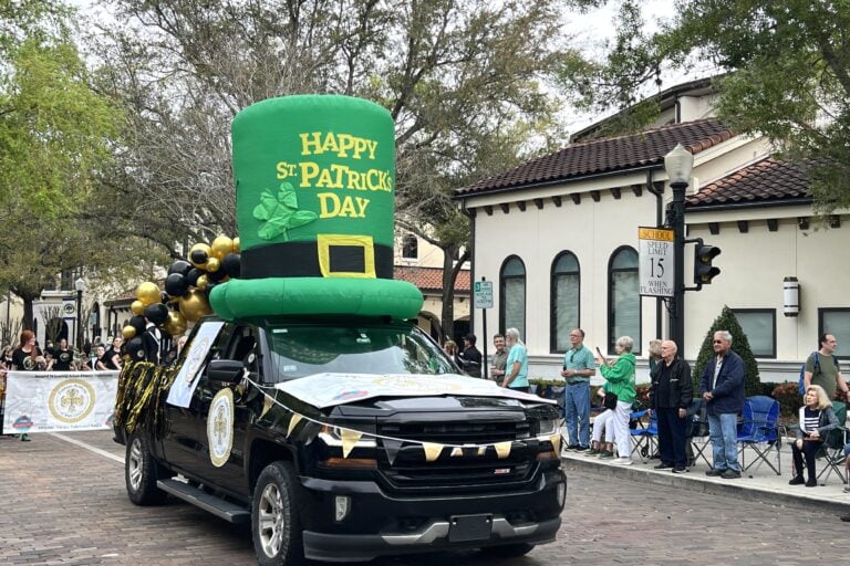 a black truck with a big inflatable on the top of roof that is a green top hat that says Happy St. Patrick's Day