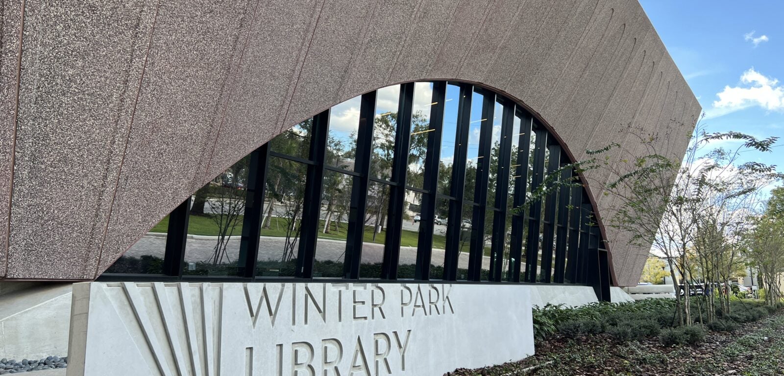 a picture of the outside building of the Winter Park Library. In front of the building is a sign that says "Winter Park Library"