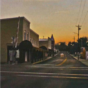 a photo of a street with an oncoming cars and building on the left of the street.