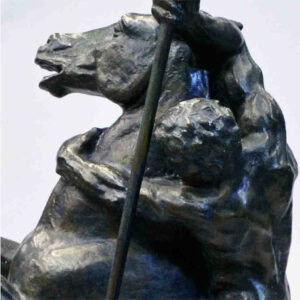 A sculpture of a warrior seated on a horse, holding a spear upright. The warrior and horse are facing backward. The sculpture stands on a rectangular base. The piece has a textured, detailed surface.