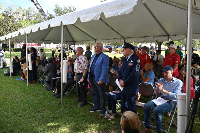 Veterans standing up in the audience while non-veterans sit down honoring those who served.