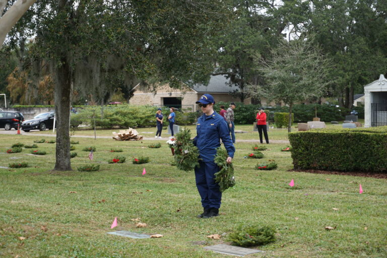 A woman standing in front of a veterans grave about to place a wreath down.