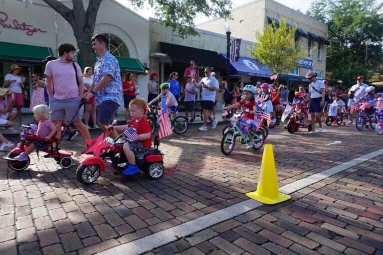 kids riding decorated fourth of july themed bikes riding on a brick road.
