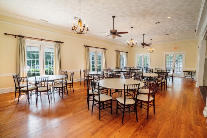 Bright event room in Winter Park, Florida with large windows, wooden flooring, elegant chandeliers, and a cozy fireplace, ideal for community gatherings and city celebrations.