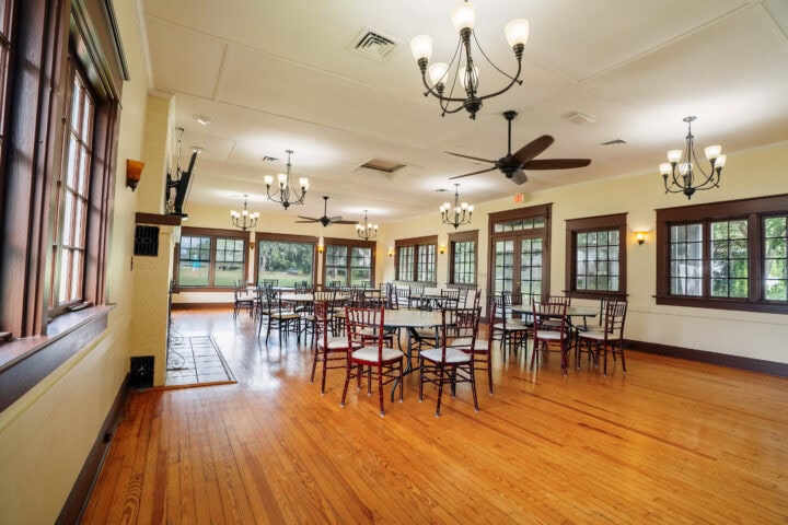Spacious event room in Winter Park with wooden floors, large windows, elegant chandeliers, and round tables, perfect for gatherings and celebrations