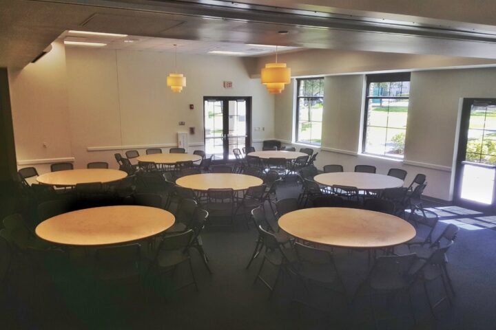 Cedar Room event set-up with round tables and black chairs, large windows providing natural light, suitable for gatherings or meetings