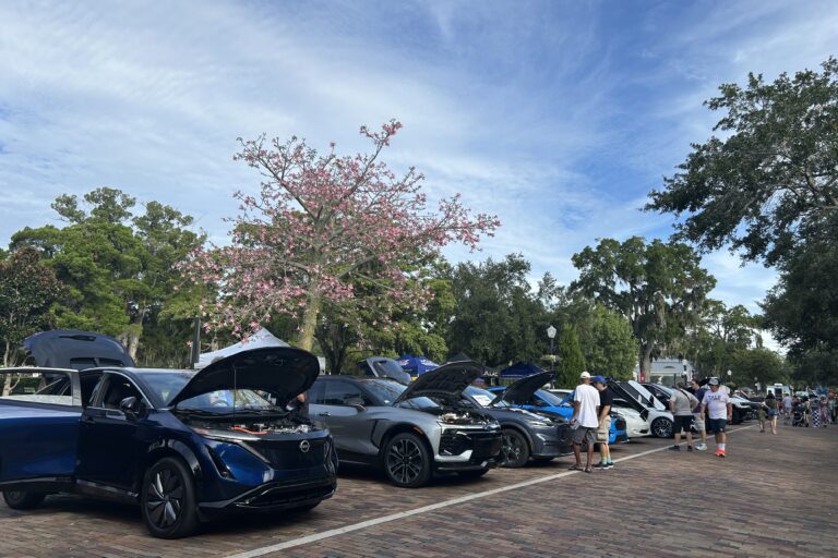 Classic car show in Winter Park with vintage vehicles on display, visitors enjoying outdoor event under blooming trees and clear sky in historic downtown area.