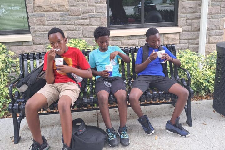 three boys sitting on a bench eating ice cream.