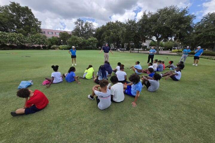Kids sitting on the grass during a youth outdoor learning session at Winter Park park, with instructors providing guidance.