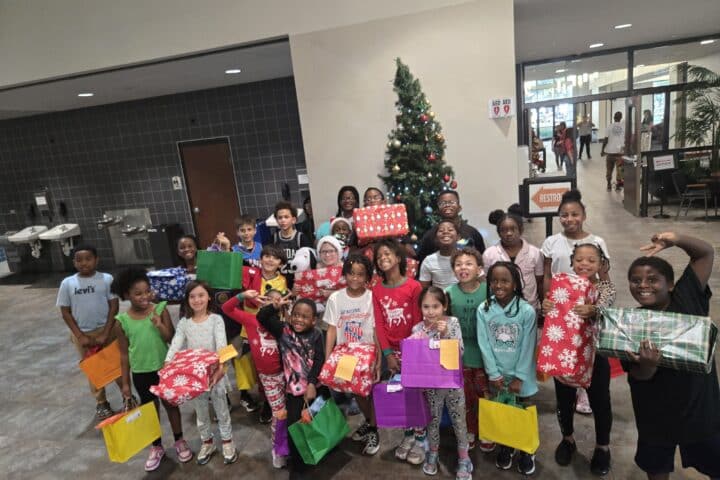 Children holding wrapped presents around a Christmas tree at a Winter Park community gathering, highlighting holiday festivities and local event participation.