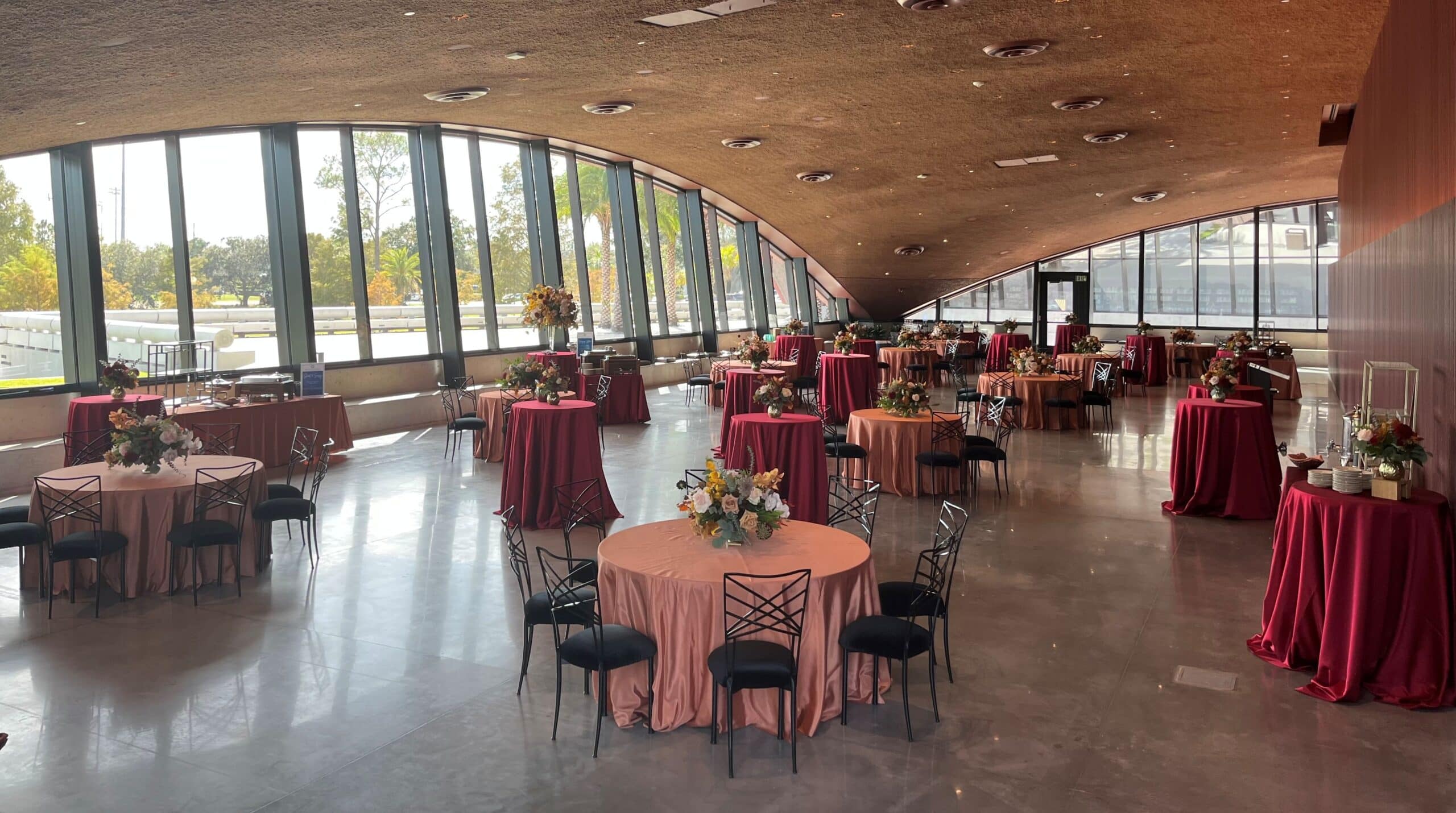 Elegant event space in Winter Park with large windows, floral arrangements, and round tables covered with pink and burgundy tablecloths, perfect for weddings and receptions.