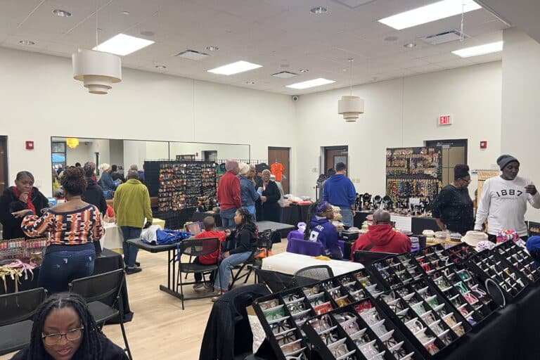 A room full of tables with products on it with people browsing the tables.