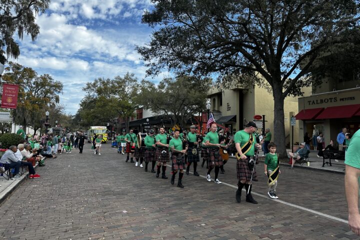People lining a brick road with bagpipers walking by for St. Patrick's Day Parade