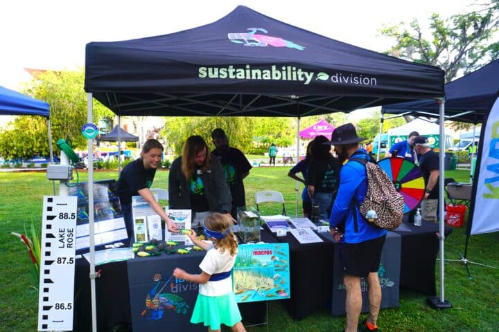 A child visits a Sustainability Division booth with staff, displays, and games at a city celebration environmental event.