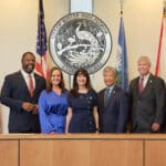 Five City Commission members in formal attire stand smiling before the Winter Park, Florida city seal and several flags.
