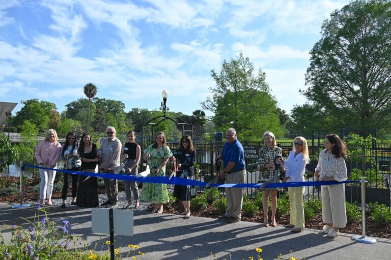 A group gathers behind a blue ribbon at the MLK Jr. Park Learning Garden ribbon cutting ceremony.