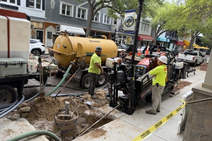 Workers in safety gear use drilling equipment and a VacCon truck for the Park Avenue Refresh at a taped-off city sidewalk site.