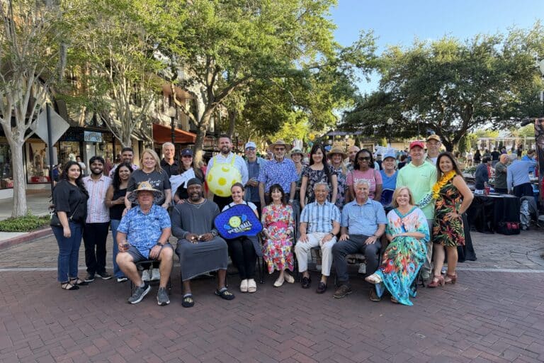 A large group poses outdoors at Dinner on the Avenue 2026, smiling with trees and buildings in the background.