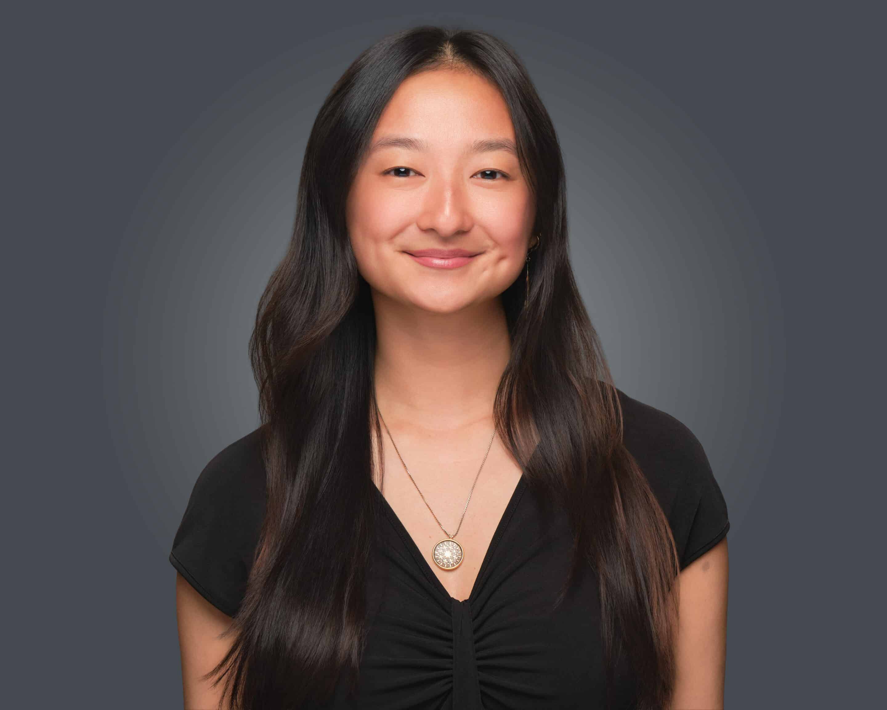 A woman with long dark hair in a black top smiles at the camera, representing the Sustainability Division.