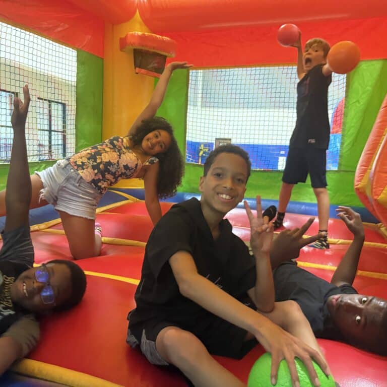 Five kids play and pose energetically inside a colorful inflatable bounce house at the community center.