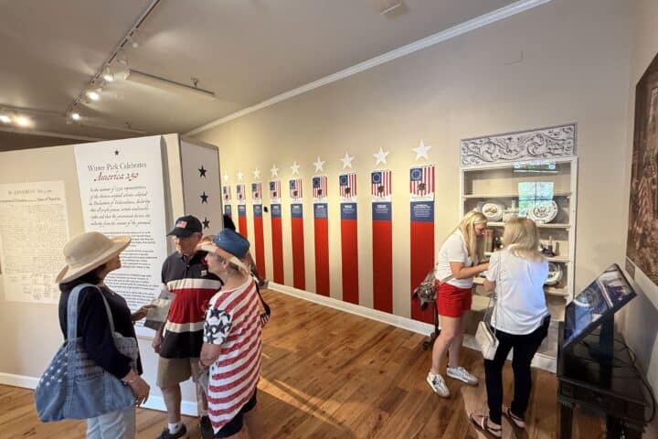 A group of people view patriotic displays and artifacts in a museum with a red, white, and blue theme.