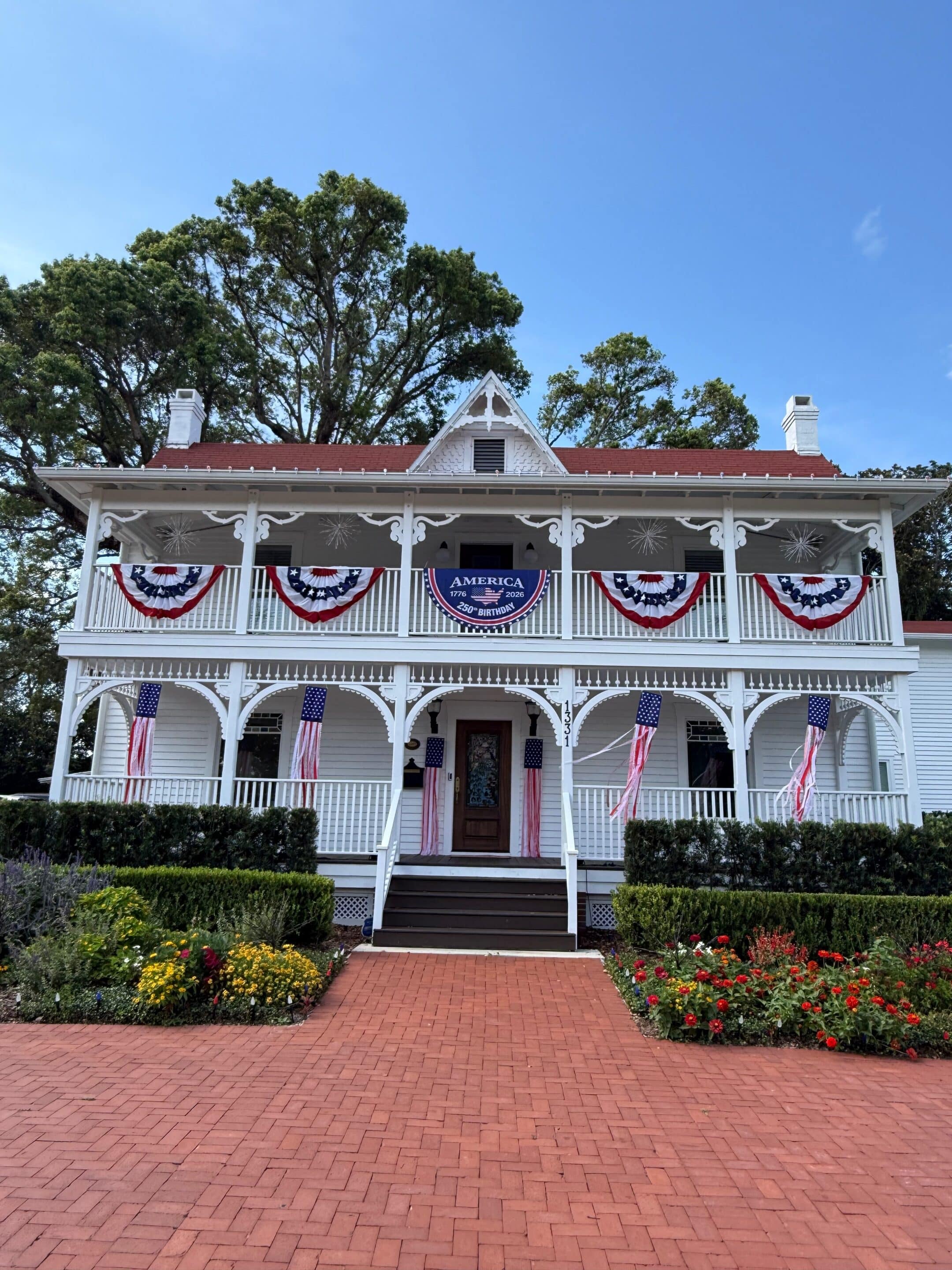 White two-story house decorated with American flags and red, white, and blue bunting for a patriotic celebration.