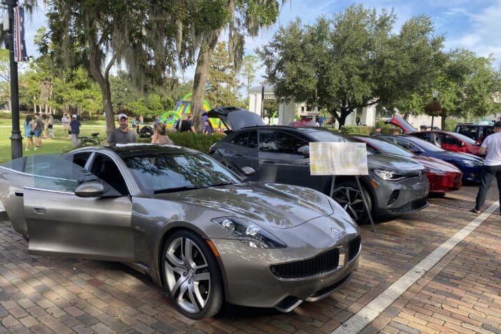 Gray sports car at the Electric Avenue EV Car Show, showcased with other cars among trees highlighting sustainability.